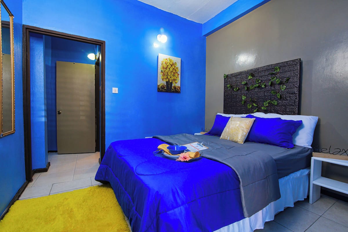 Une chambre à coucher comprenant un lit, une table de chevet, une commode, une œuvre d’art accrochée au mur et une porte.