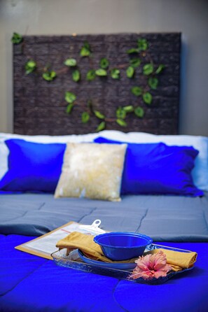 Una cama con ropa de cama azul, una almohada blanca y un cuenco azul sobre una bandeja.