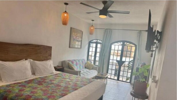 A bedroom with a large bed, a ceiling fan, and a view of the outside through a window.