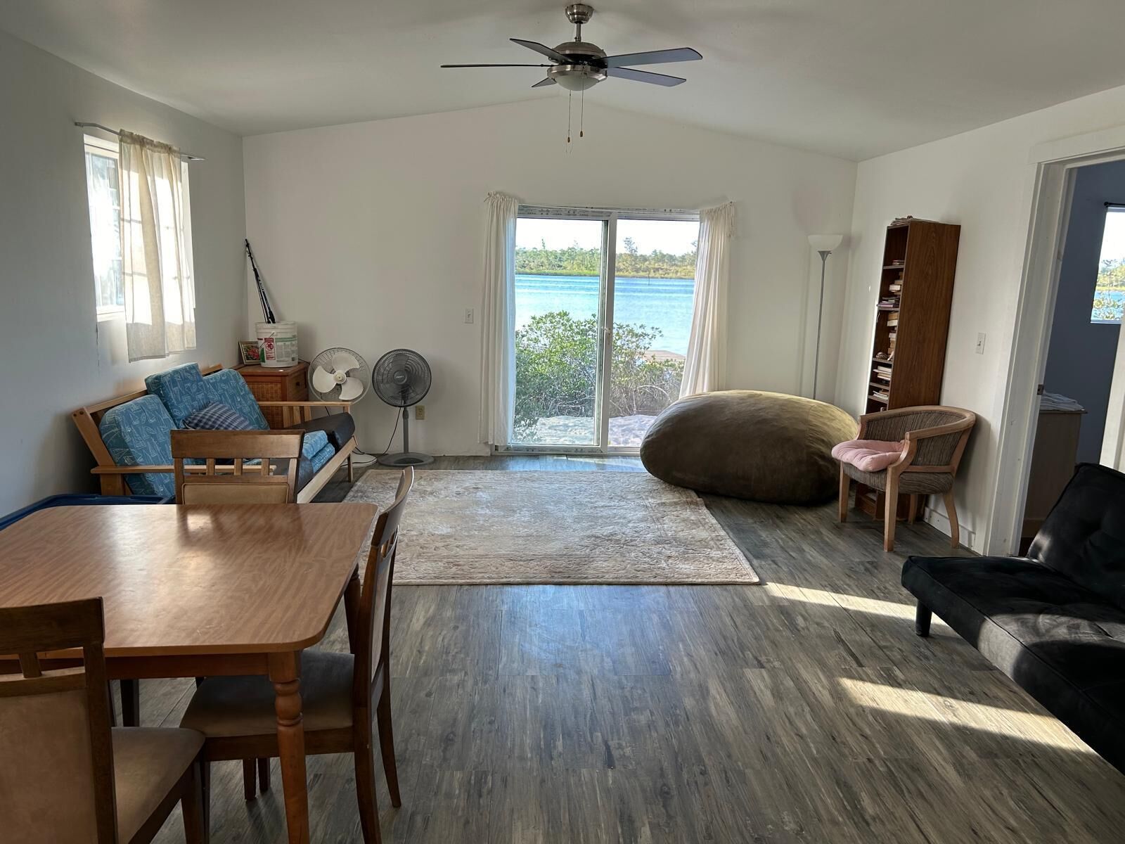 Un salón amplio con una mesa de comedor de madera, un sofá, un sofá de cuero negro y un ventanal con vistas al mar.