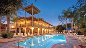 Un hotel con piscina, mobiliario exterior y una zona cubierta con luces.
