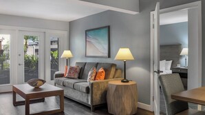 Una sala de estar moderna con un sofá gris, dos mesitas de noche con lámparas, una mesa de centro de madera y un cuadro en la pared.
