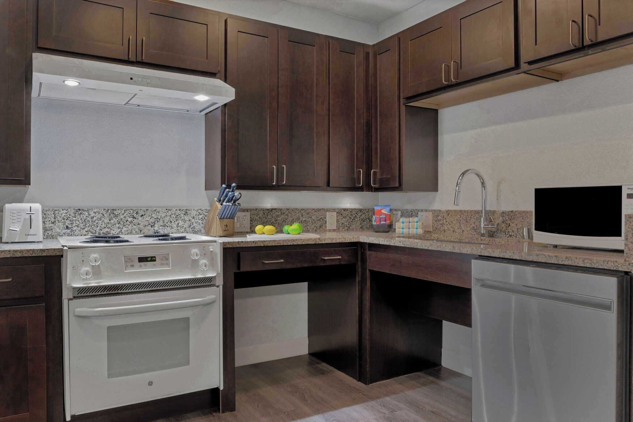 Una cucina con mobili in legno scuro, piano cottura bianco, lavastoviglie e ripiani in granito.