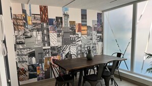 A modern office space with a large window, a wooden table with chairs, and a cityscape mural on the wall. - Apartment w/private parking, steps from Teatro Caupolicán and minutes from Movistar. (Santiago)