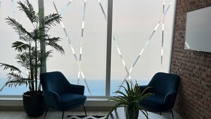 A modern office space with two blue chairs, a black and white zigzag rug, a potted plant, and a large window with a view of the sky. - Apartment w/private parking, steps from Teatro Caupolicán and minutes from Movistar. (Santiago)