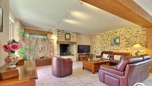 A living room with a stone wall, a fireplace, a leather sofa, a coffee table, and a TV. - Saint Co - SARZEAU - Gîte (SARZEAU)