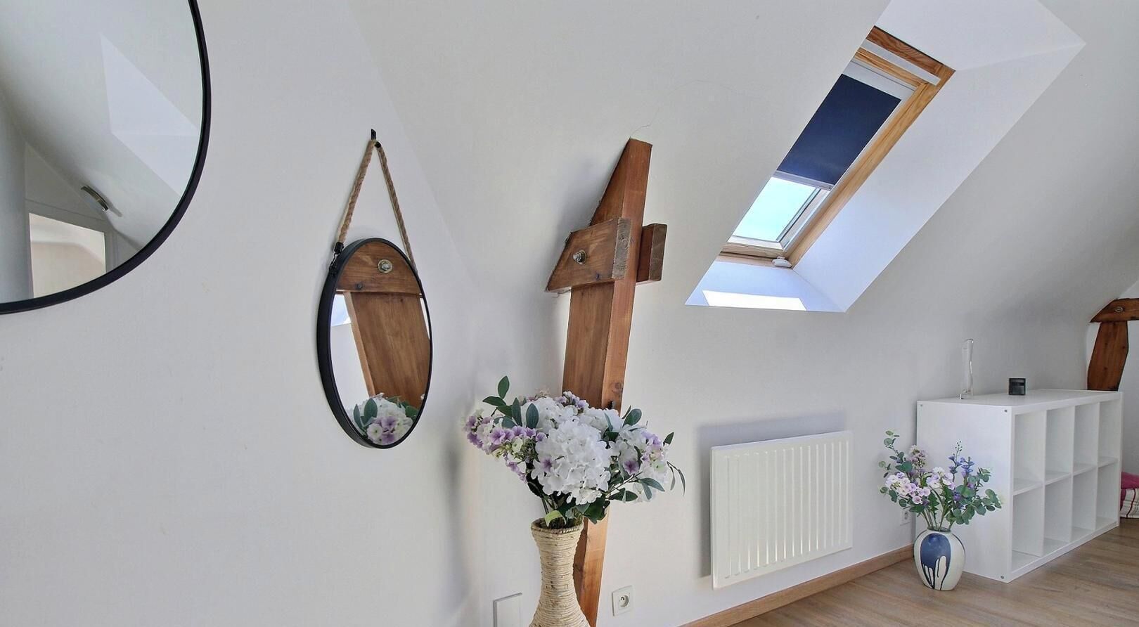 Ein Zimmer mit Dachfenster, einem Spiegel, einem Holzregal und einer weißen Heizung.