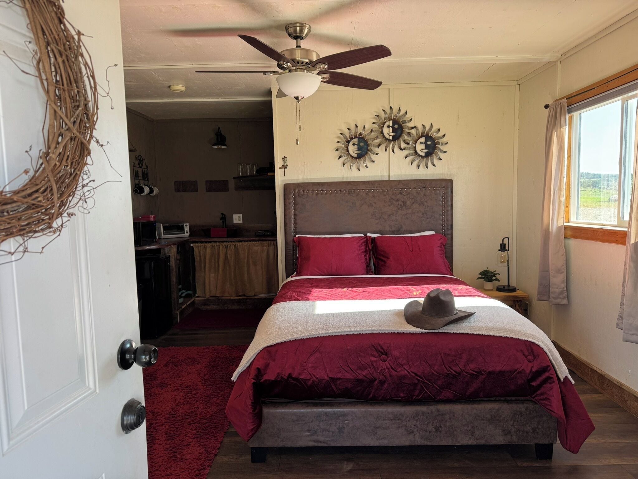 Une chambre à coucher avec un lit, un ventilateur de plafond, une fenêtre avec des rideaux et des éléments de décoration murale.