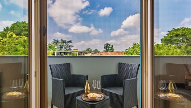A balcony with two wicker chairs, a small table with a bottle and glasses, and a view of a green landscape. - Modern apartment just a 20-minute walk from the historic center of Lucca (Lucca)
