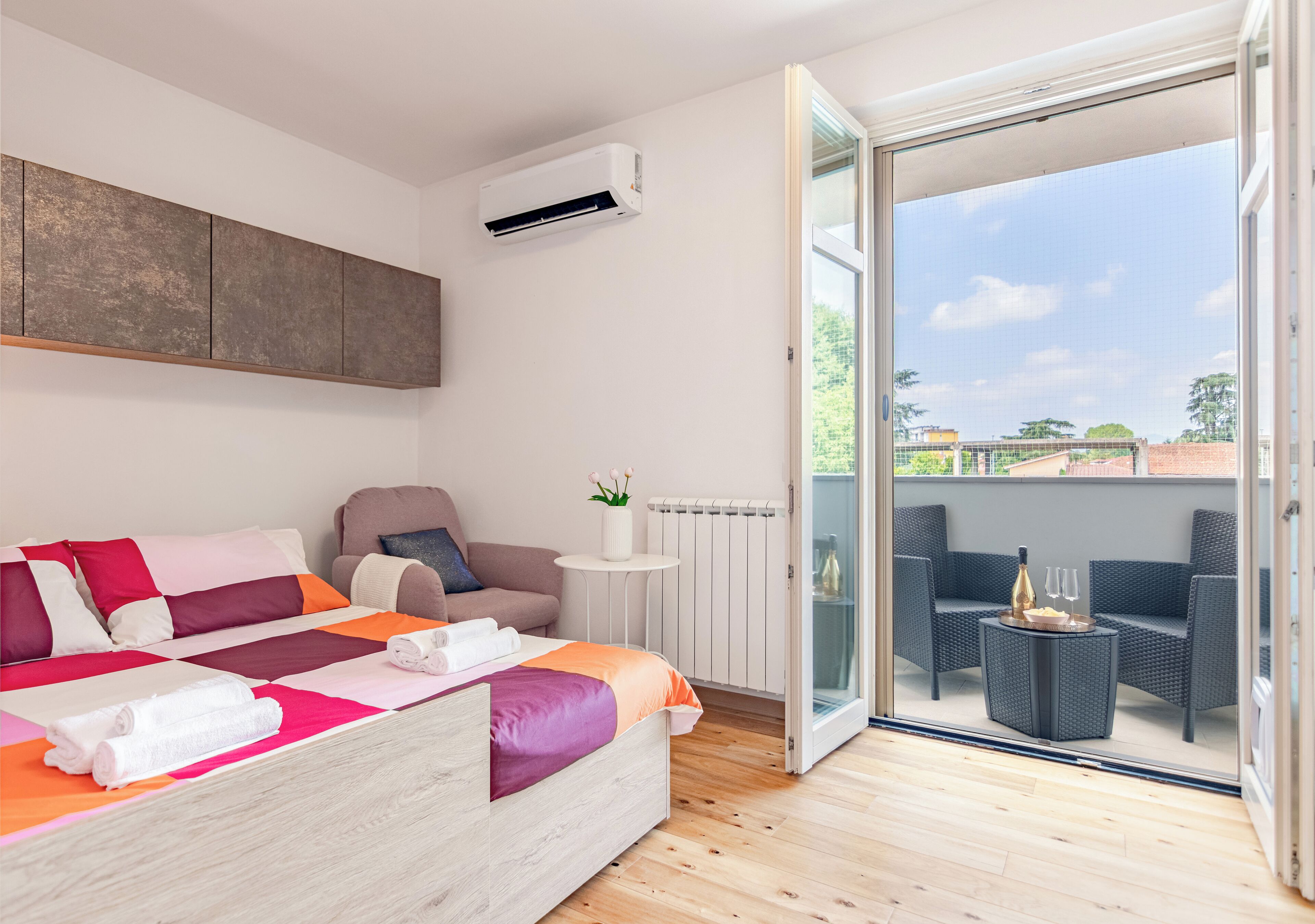 A modern bedroom with a bed, a chair, a small table, and a view of the outdoors through a glass door.
