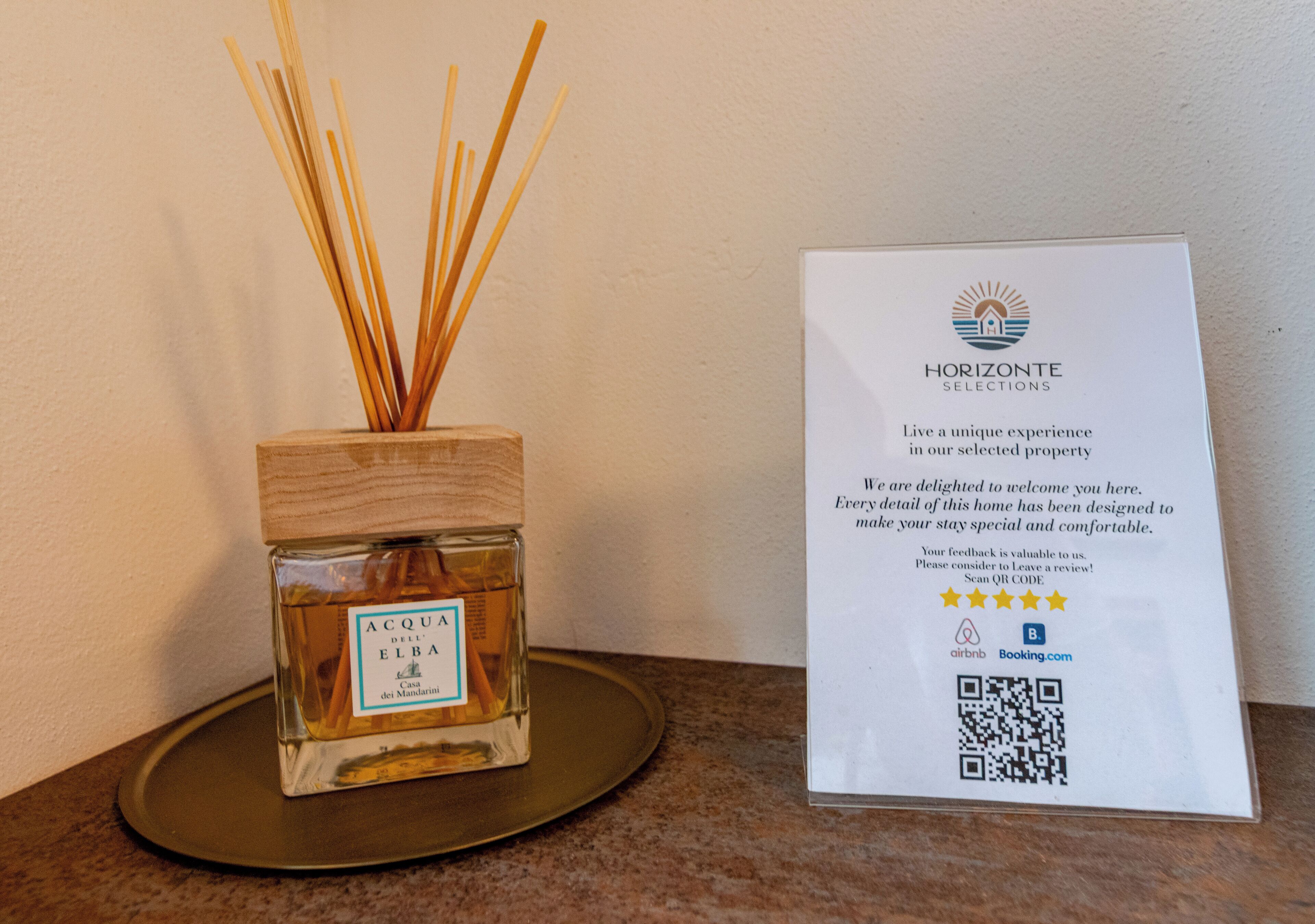 A bottle of Acqua dell'Elba on a wooden tray with reed sticks, next to a welcome sign for Horizonte Selections.