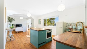 A modern kitchen with teal cabinetry, a wooden countertop, and a built-in oven. There is a window providing natural light and a view of the outdoors. - 53 Long Point, Potato Point - Hidden Coastal Retreat (Potato Point)