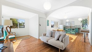 A modern living room with a sofa, a dining table, and a kitchen area with a green cabinet. - 53 Long Point, Potato Point - Hidden Coastal Retreat (Potato Point)
