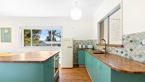 A kitchen with teal cabinets, a wooden countertop, a white refrigerator, and a view of the outside. - 53 Long Point, Potato Point - Hidden Coastal Retreat (Potato Point)