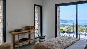 A bedroom with a large bed, a wooden desk, and a view of the sea.