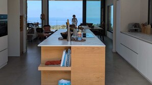A modern kitchen with a central island, large windows, and a view of the sea.
