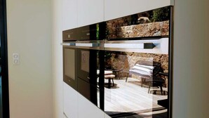 A modern kitchen with built-in appliances, a wooden ceiling, and a view of an outdoor patio area.