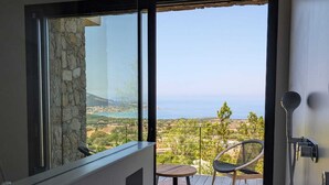 A balcony with a view of a coastal landscape, a table, and a chair.