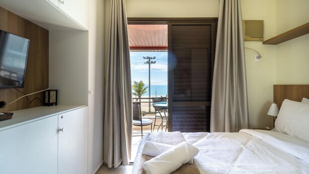 A hotel room with a bed, a TV, a balcony with a table and chairs, and a view of the sea.