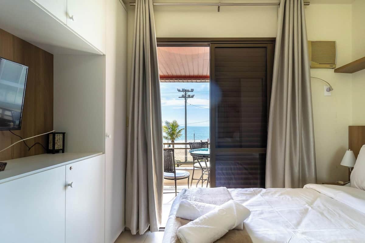 A hotel room with a bed, a TV, a balcony with a table and chairs, and a view of the sea.