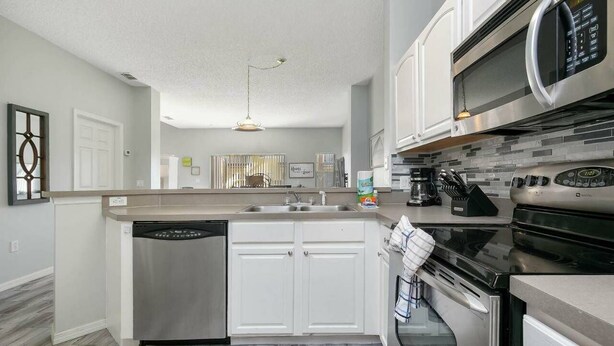 A modern kitchen with white cabinetry, stainless steel appliances, and a built-in dishwasher. - Quiet Resort 3BR Nature Walk 20min to Disney (Kissimmee)