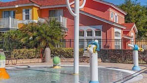 A swimming pool area with colorful dolphin sculptures, a tiled walkway, and a red building in the background. - Quiet Resort 3BR Nature Walk 20min to Disney (Kissimmee)