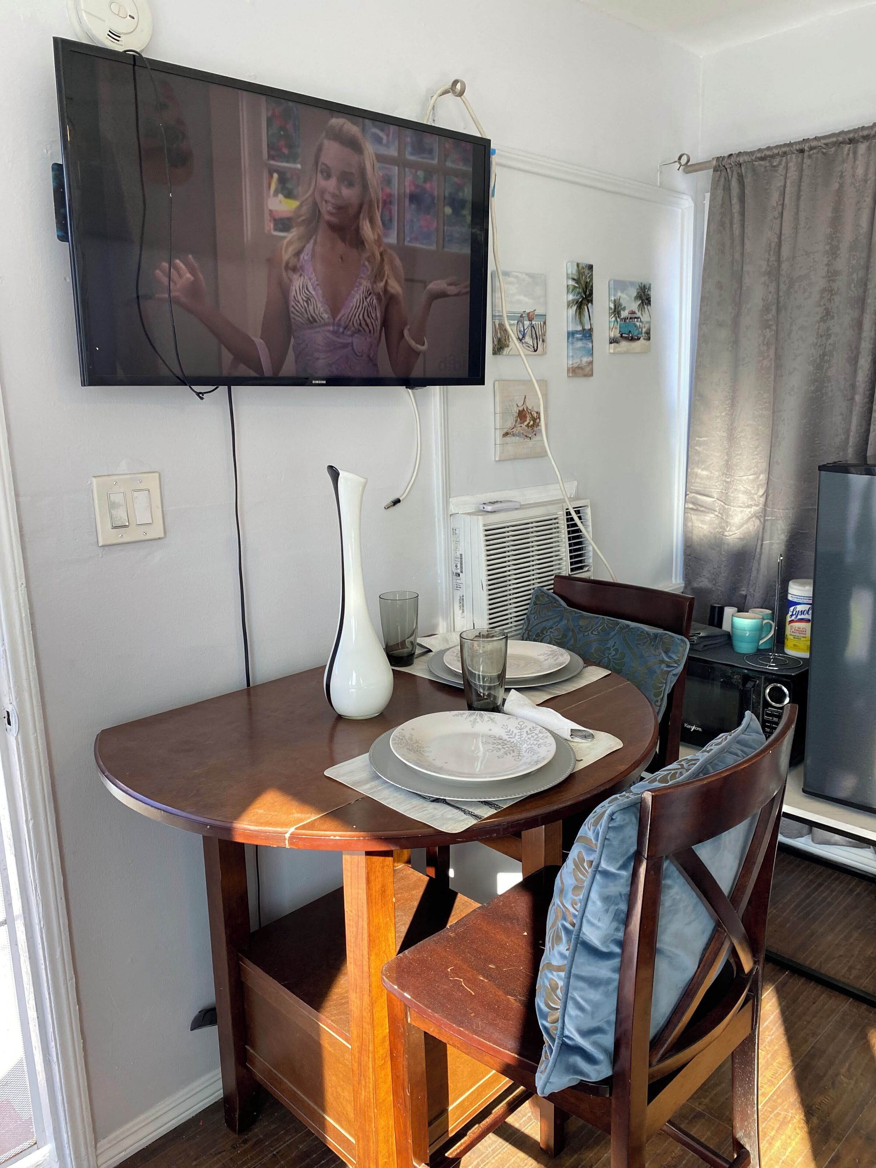 Un coin repas avec un téléviseur fixé au mur, un vase blanc et une table dressée pour deux personnes.