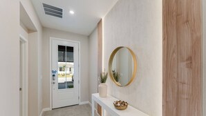 Un pasillo con una puerta blanca, una consola blanca con espejo y un florero, y una pared de acento de madera.