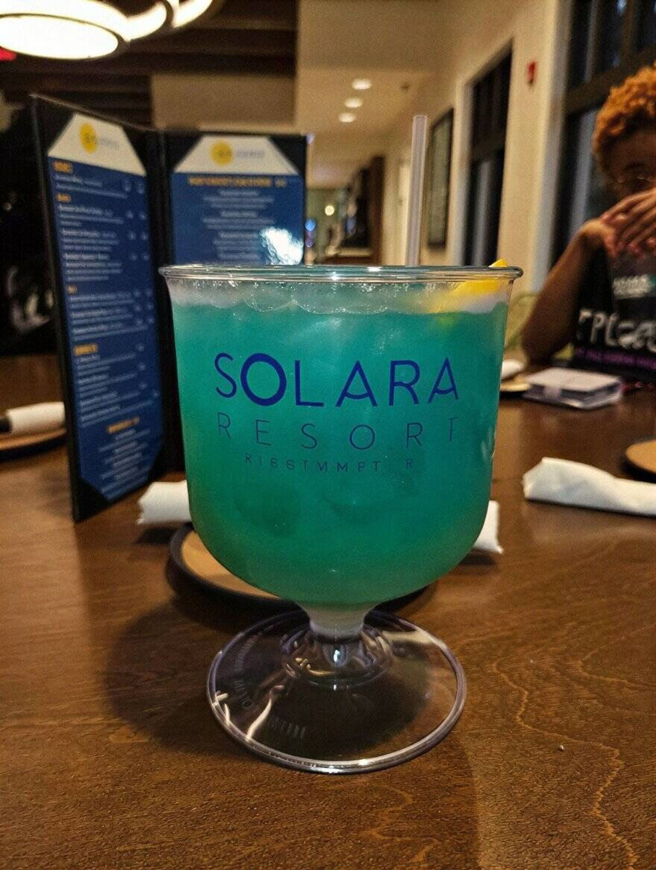 Un verre à cocktail portant l’inscription « SOLARA RESORT » est posé sur une table en bois.