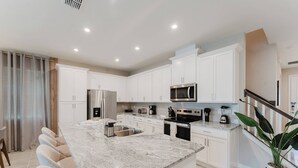 Una cocina moderna con gabinetes blancos, electrodomésticos de acero inoxidable, encimera de mármol y una isla integrada con taburetes de bar.