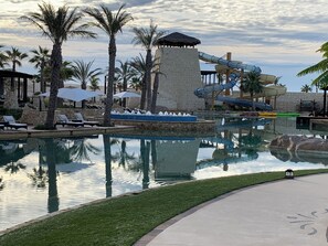 A pool area with lounge chairs, palm trees, a water slide, and a stone structure. - 2-bedroom resort in wonderful Cabo San Lucas next to Solmar Links golf course! (Cabo San Lucas)