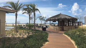 Ein Strandresort mit einem Gazebo mit Reetdach, Liegestühlen und einer Holzpromenade, die zum Strand führt.