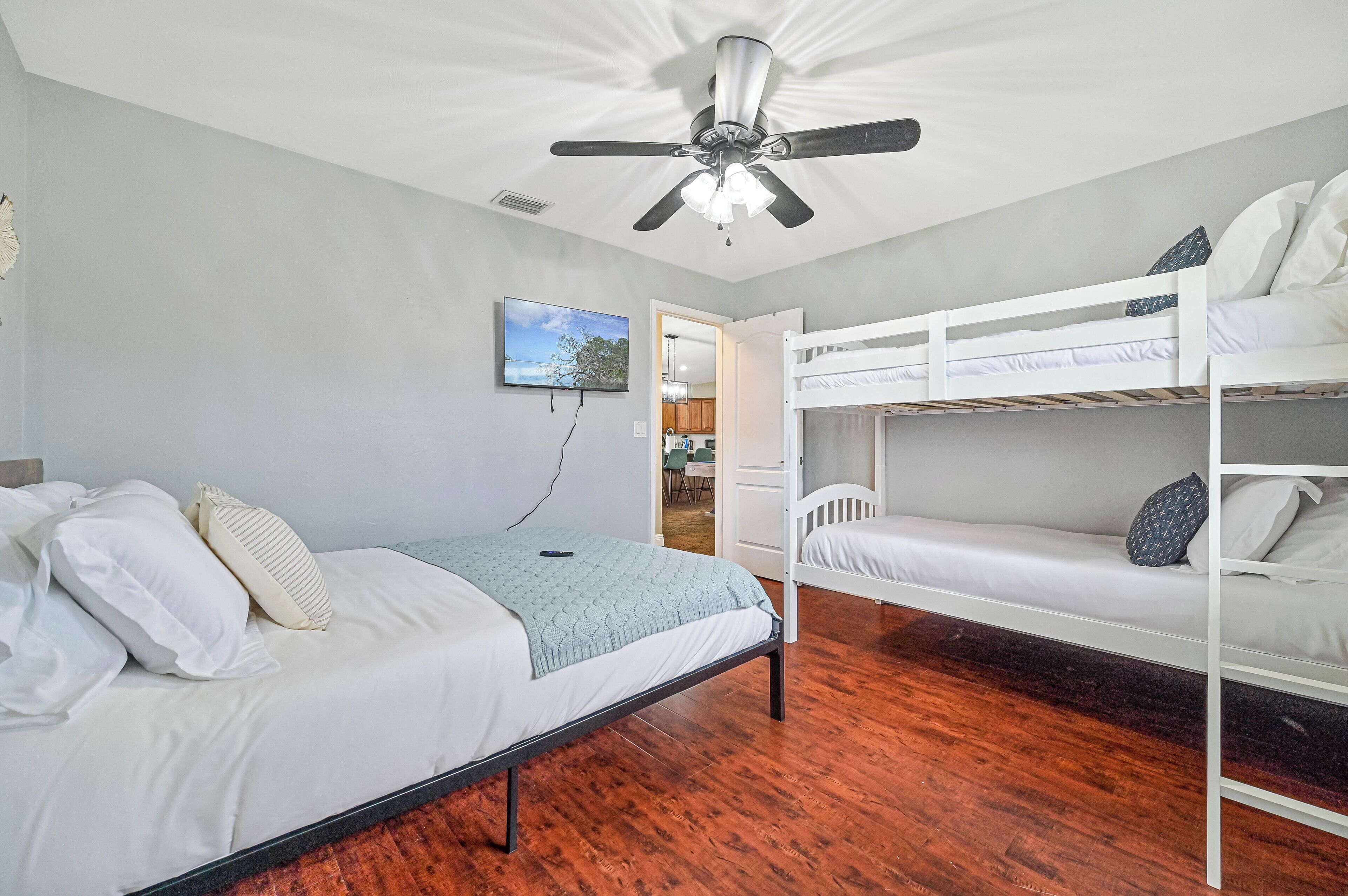 Una habitación con una cama individual, una cama litera, un ventilador de techo y vista a la cocina.