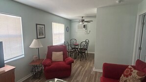 Un salon avec un canapé rouge, une table basse en verre et un coin repas comprenant une table et des chaises.