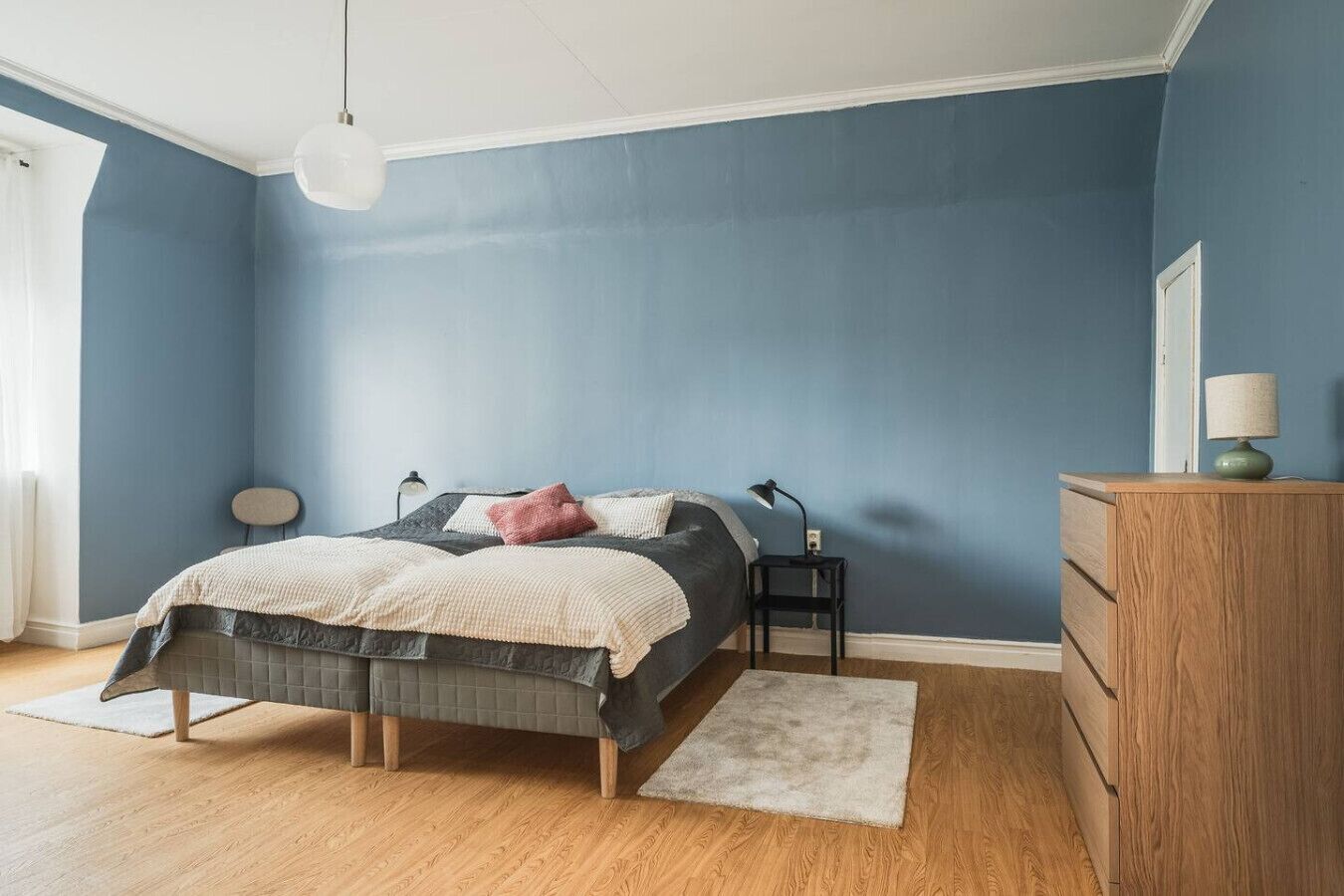A bedroom with a bed, bedside tables, a dresser, and a hanging light fixture.