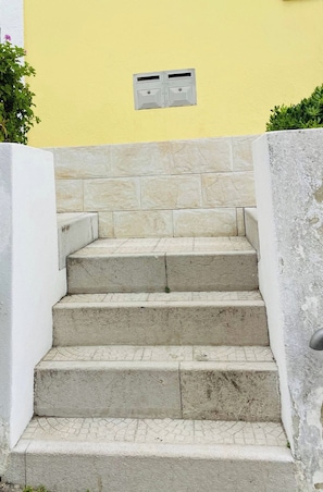 A set of concrete steps leading up to a building with a yellow wall and a small ventilation unit above. - Tagus River Apartment *Cacilhas, 10min from Lisbon (Almada)