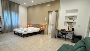 A modern hotel room with a bed, a desk, a green sofa, and a tiled floor. - RoccaRooms (Catania)