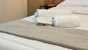 A neatly made bed with white linens and a folded towel on a textured beige blanket. - RoccaRooms (Catania)