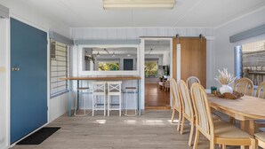 Une cuisine spacieuse avec une table et des chaises en bois, une porte bleue et une vue sur le jardin grâce à de grandes fenêtres.