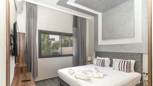 A modern hotel room with a large bed, a TV, a window with curtains, and a view of greenery outside. - Villa in the heart of Marrakech city center, with a private pool. (Marrakesh)