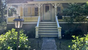 Een tweelaags huis met een veranda, een trap naar de voordeur en een omheinde tuin.