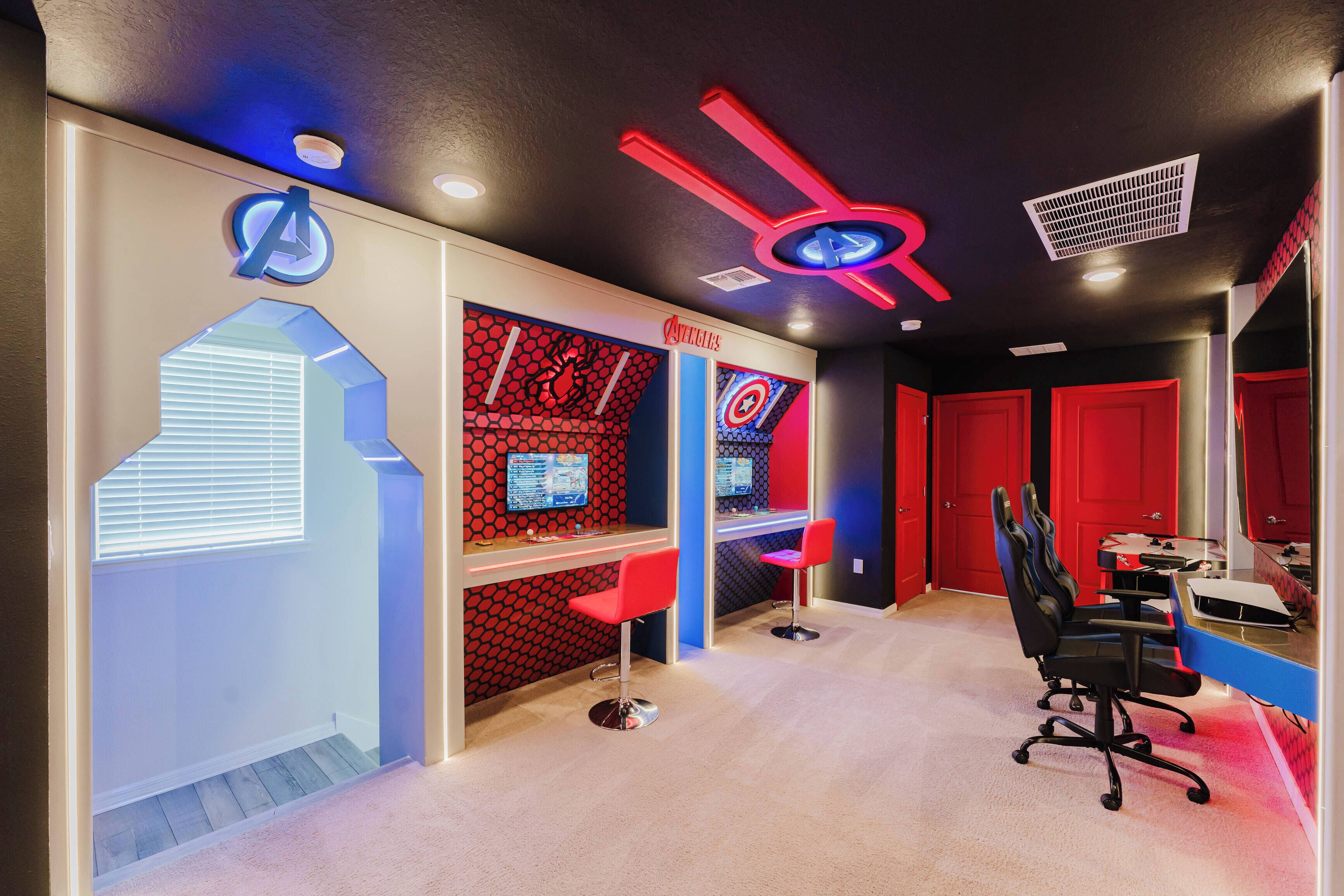 A gaming room with red and blue decor, gaming chairs, and multiple gaming stations.