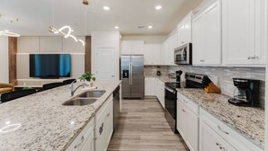A modern kitchen with white cabinets, granite countertops, stainless steel appliances, and a built-in oven. - Family 5BR Windsor Island Princess Toy Story Rooms (Davenport)