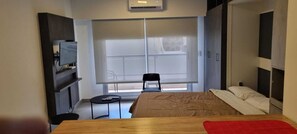 Une chambre à coucher avec un lit, une petite table, une chaise et une fenêtre avec des stores.