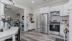 A modern kitchen with white cabinets, stainless steel appliances, and a wooden dining table. - "KOZY KOTTAGE" Near Downtown! 2025 Remodel, Sleeps 8 Comfortably, Games & More! (Denison)