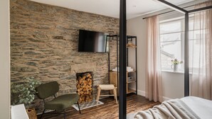 Ett sovrum med en vägg av sten, en tv, en trästol, en säng och ett fönster med gardiner.