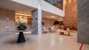 A modern hotel lobby with a reception desk, seating area, and a large screen.