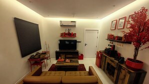 Sala de estar com sofá, televisão e um vaso com planta vermelha.
