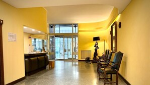 A hotel lobby with a reception desk, seating area, and a glass door entrance. - TORRE CANTORE 69 (GENOVA OVEST/PORTO)   GENOVABB.IT (GENOVA)