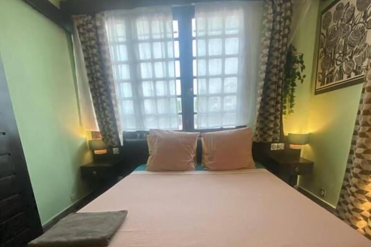 Un dormitorio con una cama, dos mesitas de noche, una ventana con cortinas y una obra de arte en la pared.